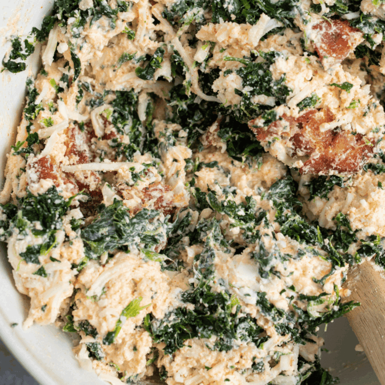Mixing bowl filled with cream cheese, mayo, sour cream, garlic, spinach, artichokes, mozzarella, and Parmesan being combined for spinach dip mixture.
