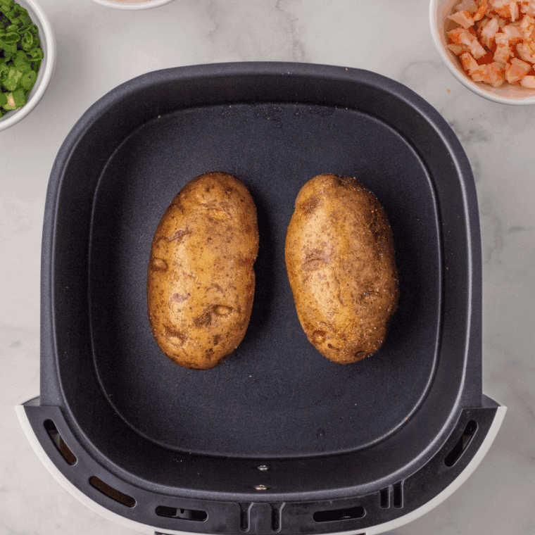 Russet potatoes coated in olive oil and salt, cooking in the air fryer until golden and tender.