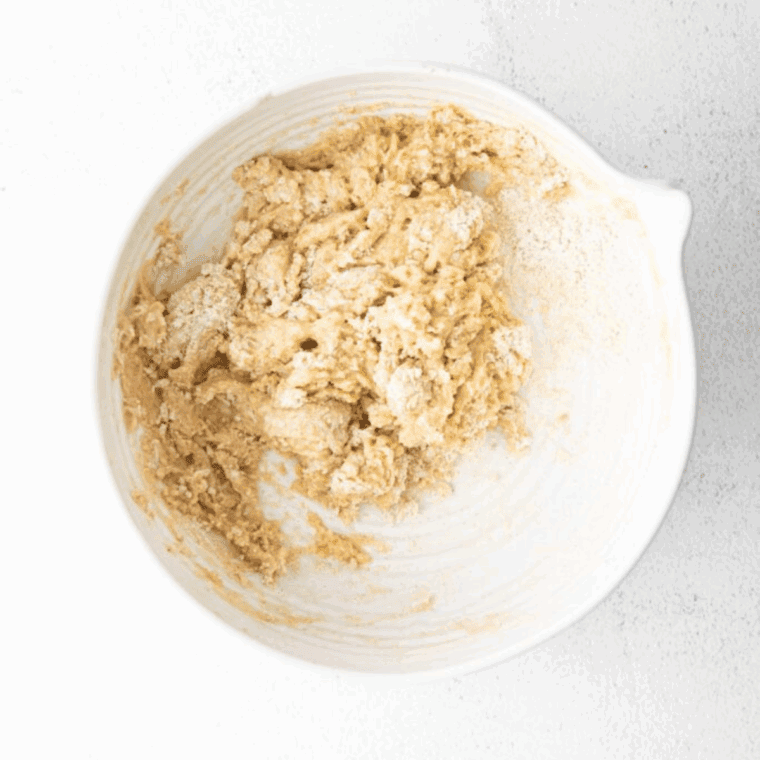 Mixing sourdough starter with wet and dry ingredients in a bowl to form thick apple fritter batter