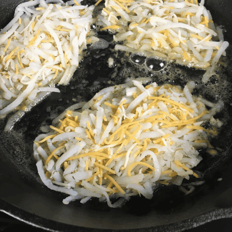 Cooking shredded potatoes in a skillet with butter and seasoning for crispy hash browns.