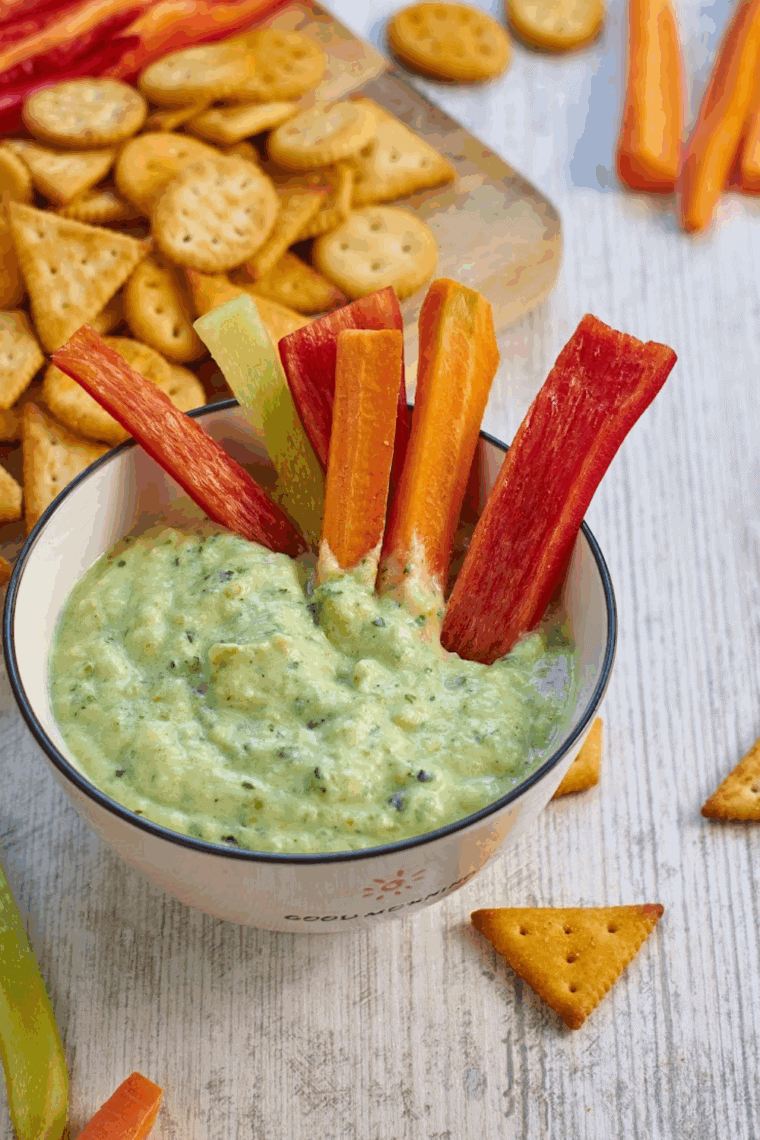 Creamy zucchini yogurt dip in a bowl garnished with herbs, served with fresh veggie sticks.