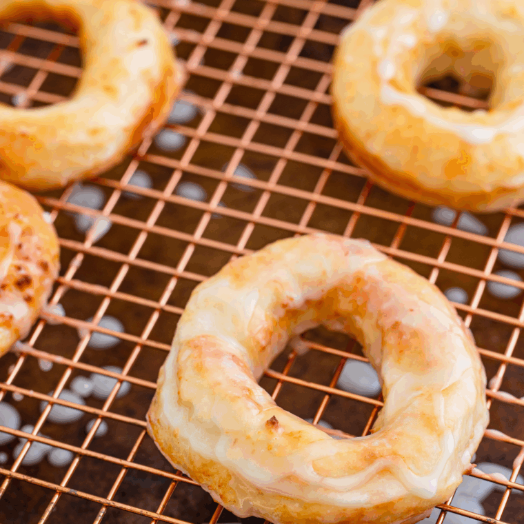 Freshly made air fryer Greek yogurt donuts with golden edges and light glaze on a cooling rack.