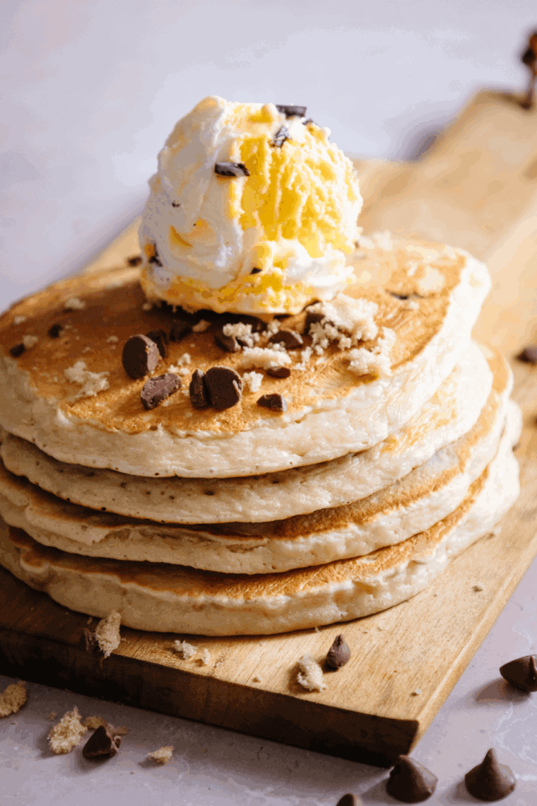 Golden banana chocolate chip pancakes made in the air fryer, piled on a plate with syrup and fresh banana slices.