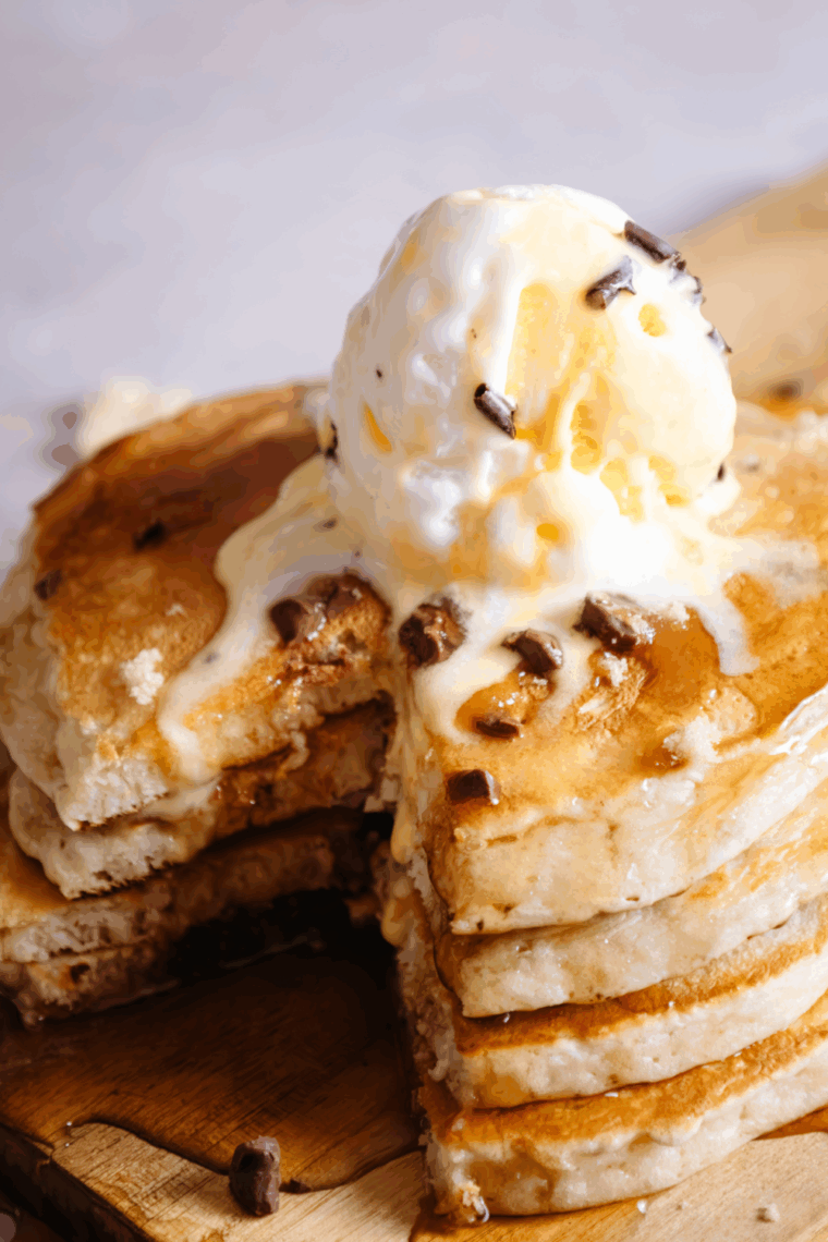 Pile of soft banana chocolate chip air fryer pancakes with syrup and added chocolate chips resting on a breakfast plate.