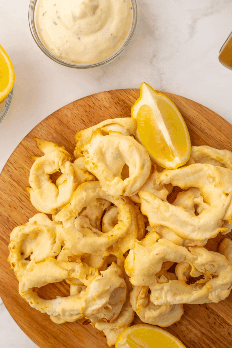 Homemade Benihana-style calamari on a plate, garnished with green onions and lemon wedges.