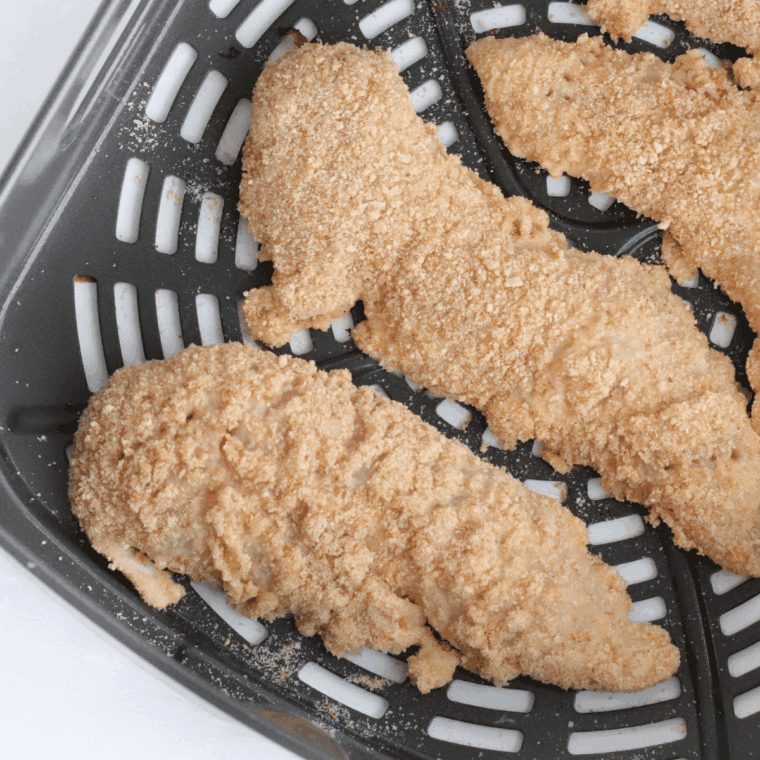 Chicken tenders breaded and cooking in an air fryer basket until crispy.