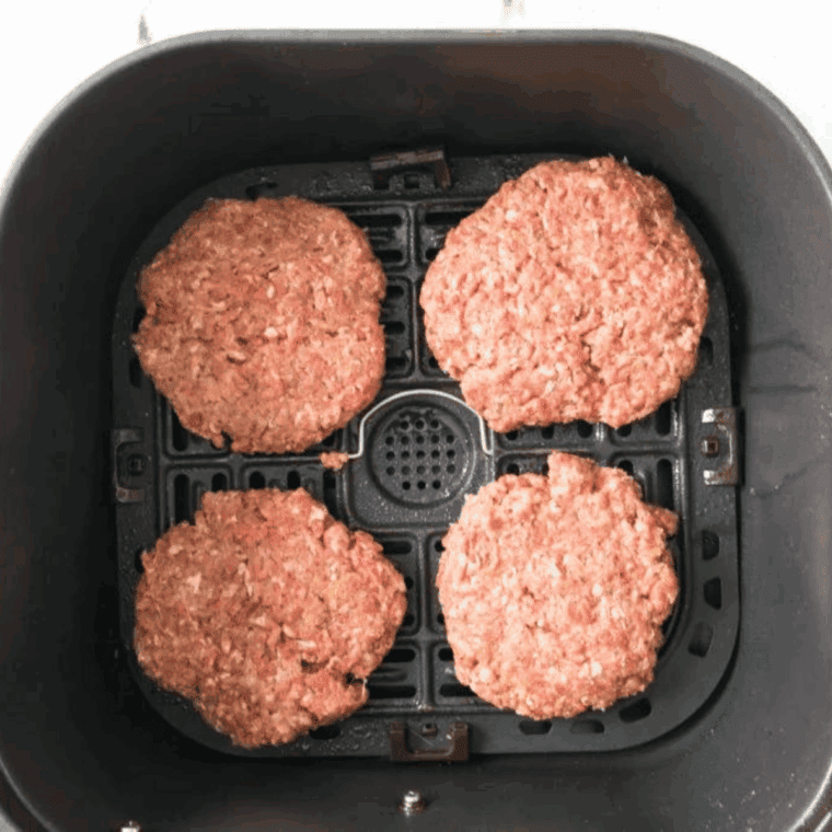 Hamburgers lined up in a single layer inside the air fryer basket, cooking at 370 degrees F until brown.