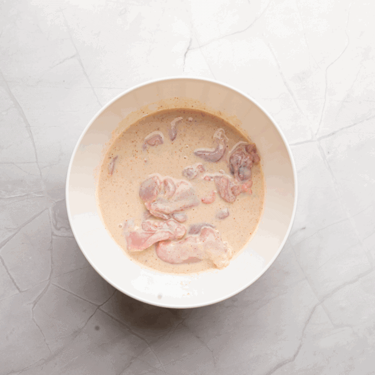 Chicken pieces soaking in buttermilk in a bowl, ready to marinate for tenderness and flavor.