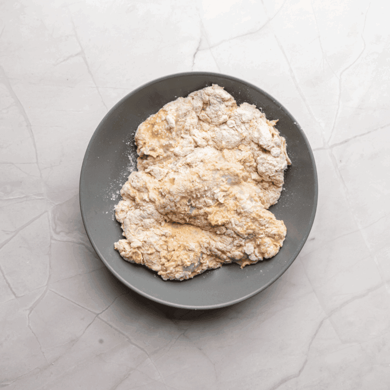 Chicken pieces being dredged in the seasoned flour mixture, coating each piece evenly.