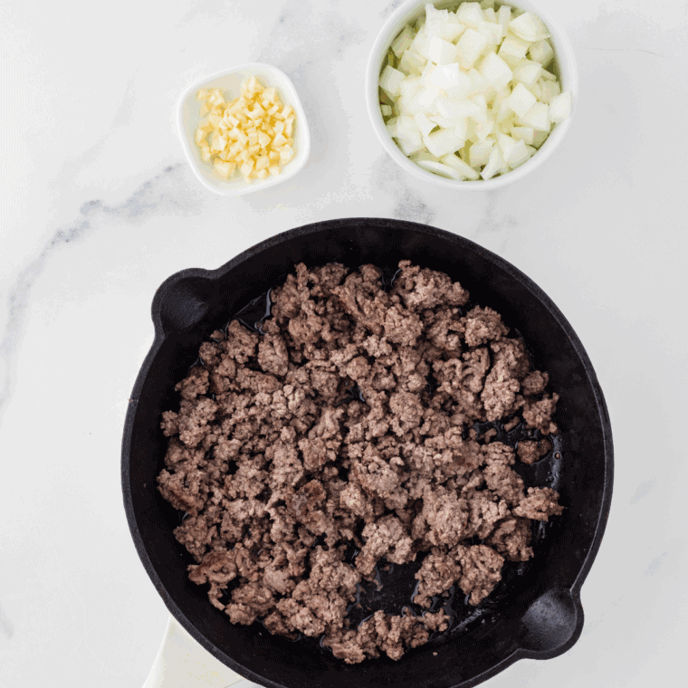 Browning ground beef in a skillet and seasoning with garlic powder, Italian seasoning, salt, and pepper.