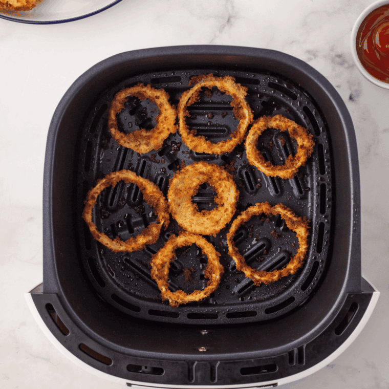 Coated onion rings arranged in an air fryer basket, ready to cook, golden and crispy after cooking
