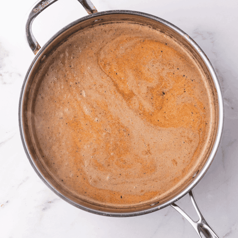 Heavy cream simmering in a skillet while being stirred gently.