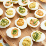 Homemade Ina Garten deviled eggs topped with paprika and fresh herbs, served on a platter for parties or holiday gatherings.