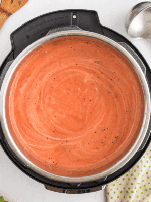 Bowl of creamy Instant Pot Madeleine Tomato Basil Soup garnished with fresh basil leaves and served with crusty bread.