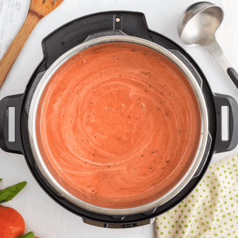 Bowl of creamy Instant Pot Madeleine Tomato Basil Soup garnished with fresh basil leaves and served with crusty bread.