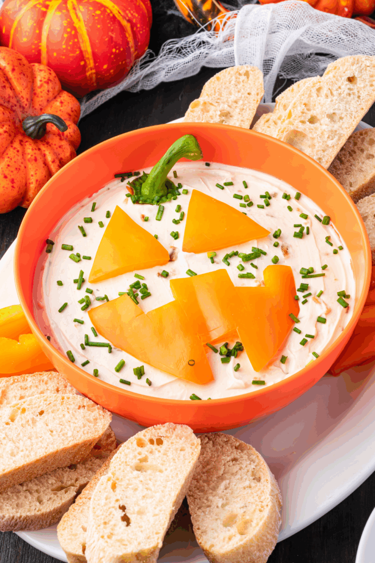 Festive Jack-O'-Lantern Onion Dip served in a carved orange pepper with crackers and veggies for dipping.