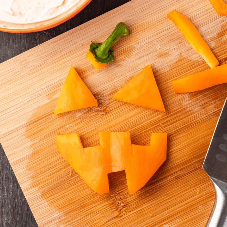Carving eyes, nose, and mouth into the onion dip for a Jack-O’-Lantern face.