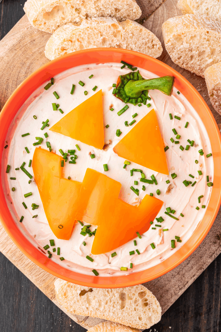 Festive Jack-O’-Lantern onion dip decorated like a pumpkin, served with crackers and veggies for dipping.
