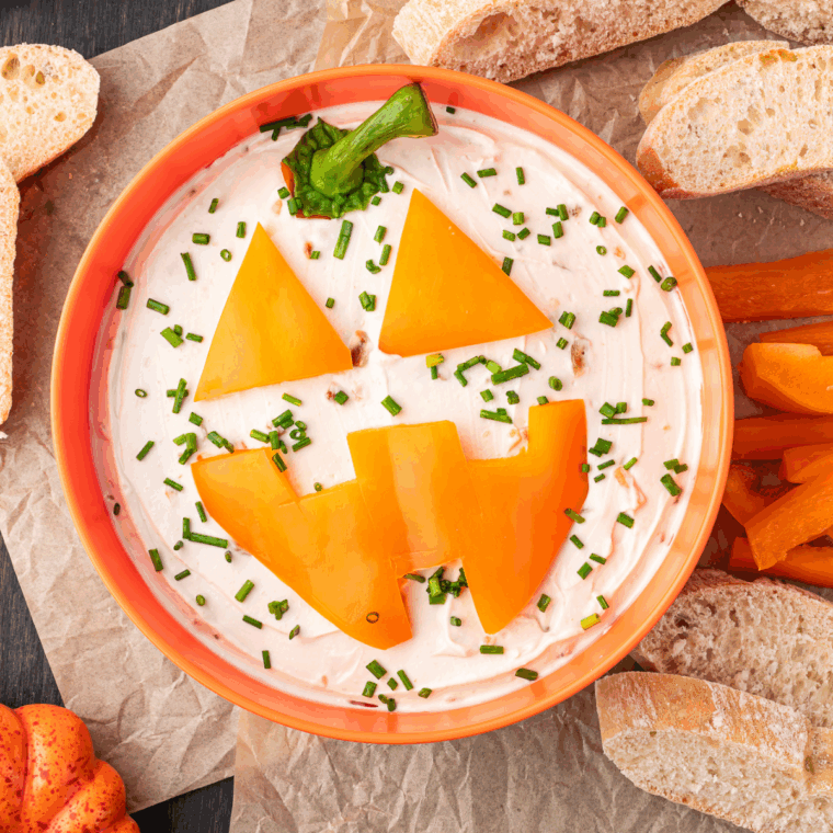 Halloween Jack-O'-Lantern onion dip served inside a carved pumpkin with chips for dipping.