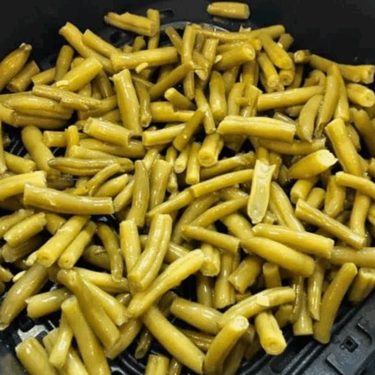 Air Fry the Green Beans: Green beans cooking in the air fryer, being shaken halfway through for even crisping.