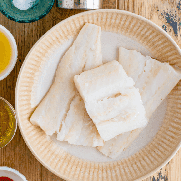 White fish fillets being patted dry and seasoned with salt and pepper.