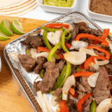 Homemade Lupe Tortilla fajitas with tender steak, sizzling peppers, onions, and warm tortillas served on a skillet.