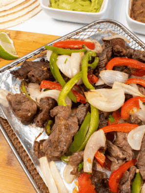 Homemade Lupe Tortilla fajitas with tender steak, sizzling peppers, onions, and warm tortillas served on a skillet.