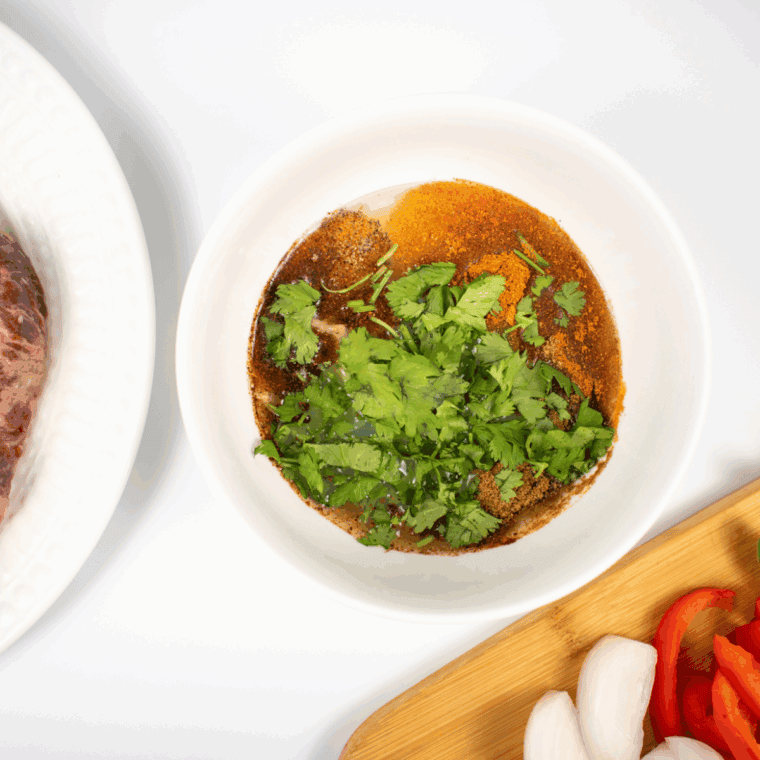 Steak marinating in a bowl with lime juice, soy sauce, garlic, and spices for Lupe Tortilla fajitas.