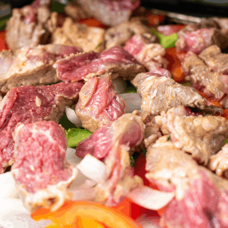 Sliced onions and bell peppers cooking in a cast iron skillet until tender and charred for fajitas.