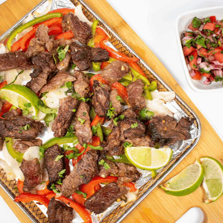 Skillet of Lupe Tortilla copycat fajitas with marinated steak, grilled onions, and colorful bell peppers.