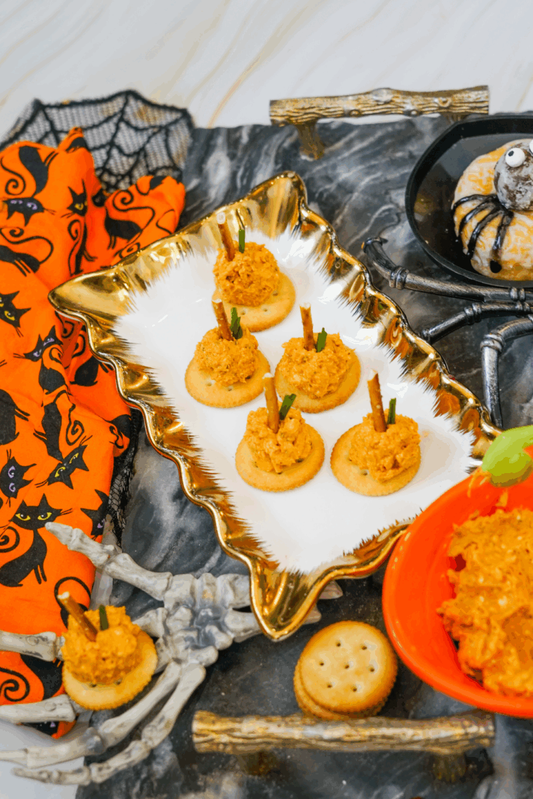 Mini pumpkin-shaped cheese balls coated with crushed cookies topped with pretzel stems and parsley leaves, placed on a festive plate.