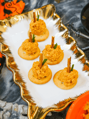 Mini pumpkin-shaped cheese balls coated in crushed crackers with pretzel stems and parsley leaves, served on a fall appetizer platter.