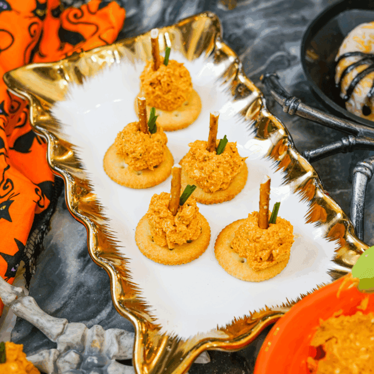 Mini pumpkin-shaped cheese balls coated in crushed crackers with pretzel stems and parsley leaves, served on a fall appetizer platter.