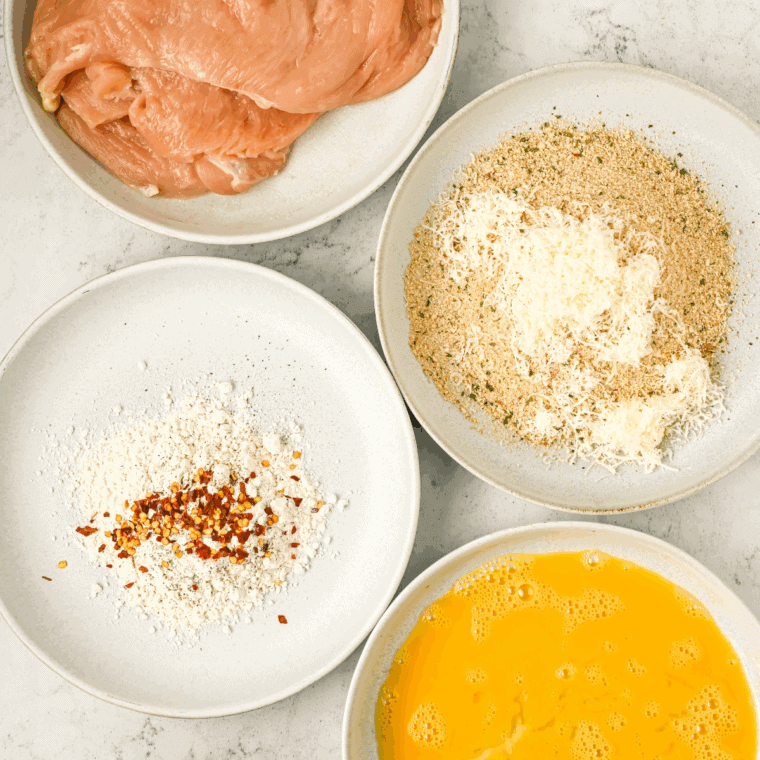Preparing three bowls with flour, beaten eggs, and breadcrumb-Parmesan mixture for chicken coating.