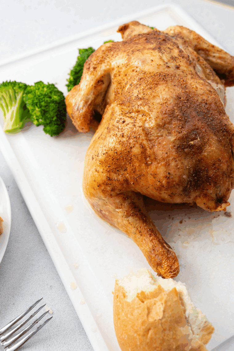 Golden roasted Barefoot Contessa Cornish Hen on a platter with herbs and lemon wedges.