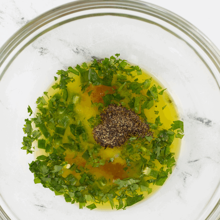 Mixing chopped parsley, basil, and minced garlic into the citrus mixture while slowly drizzling in olive oil to emulsify.
