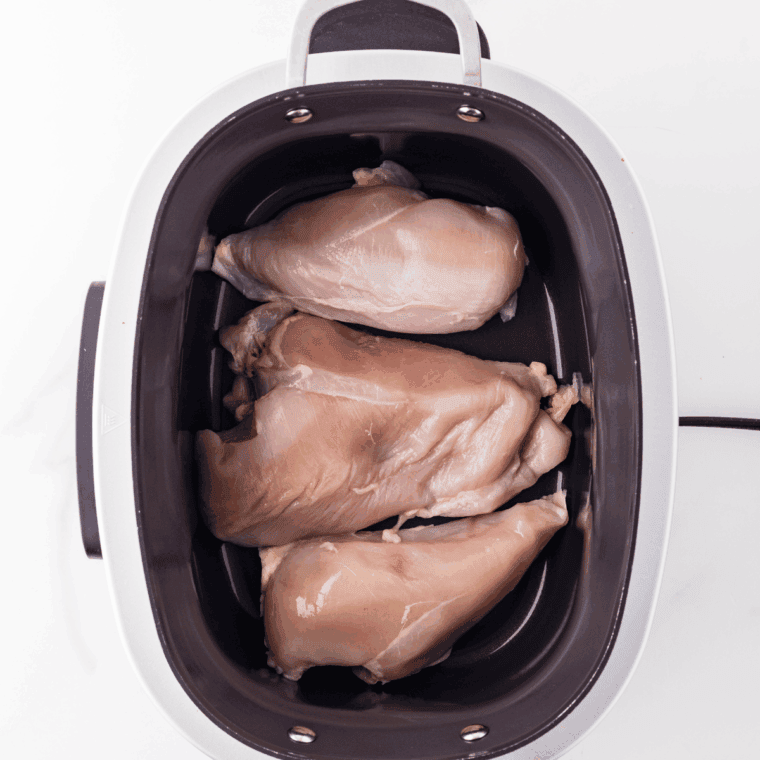 Adding chicken breasts, chicken broth, and cream of chicken soup to a crock pot.