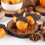 Plate of soft, spiced acorn-shaped donut holes decorated with chocolate and crushed nuts.