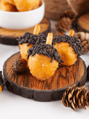 Plate of soft, spiced acorn-shaped donut holes decorated with chocolate and crushed nuts.
