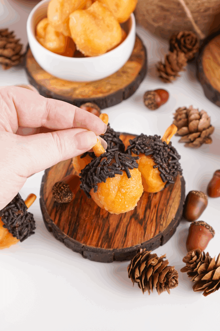 Plate of bite-sized acorn-shaped donut holes decorated with chocolate and crushed nuts, perfect for fall.