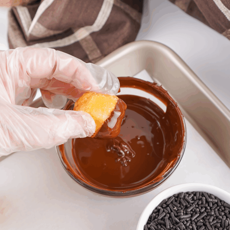 Donut hole being dipped into melted chocolate.