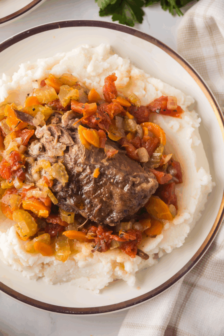 Braised lamb shanks served on a plate with rich red wine sauce and fresh herbs.