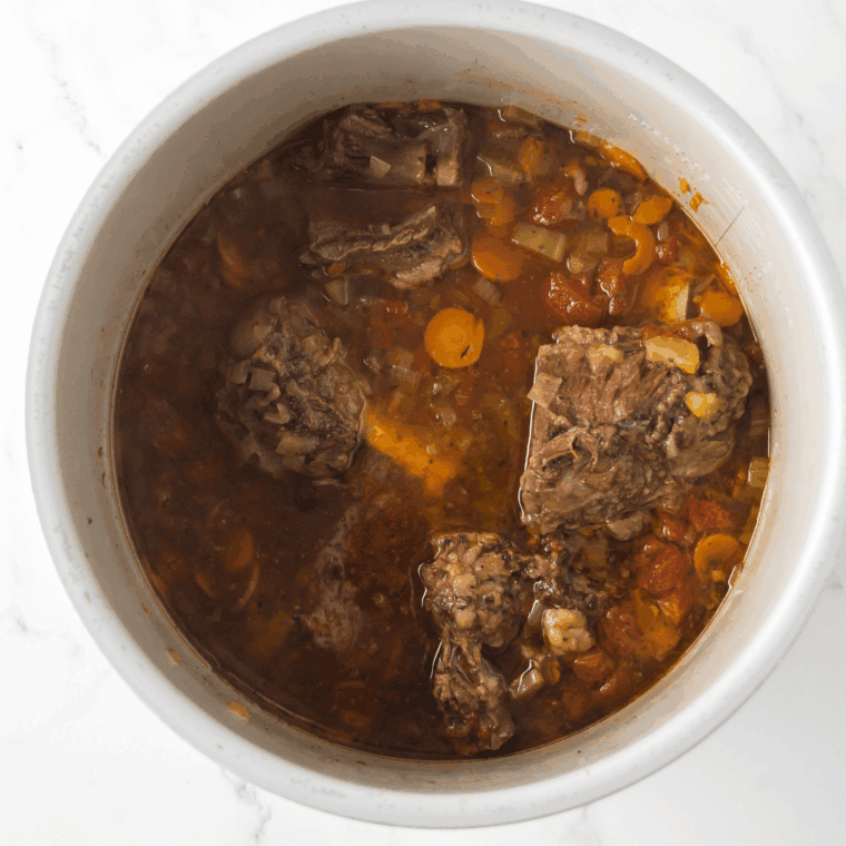 Lamb shanks simmering gently in a covered pot until tender and falling off the bone.
