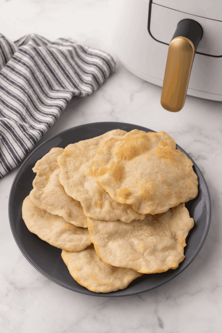 A plate of easy air fryer homemade flour tortillas on the kitchen table near the air fryer basket.