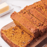 Freshly baked loaf of Easy Cardamom Pumpkin Bread sliced on a wooden board, showing its moist, spiced texture and golden-brown crust.