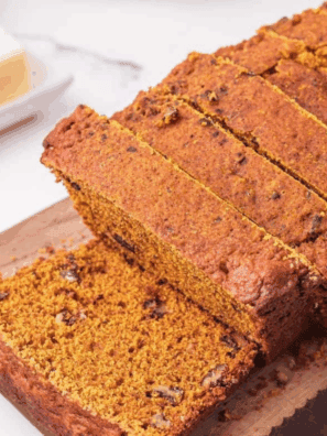 Freshly baked loaf of Easy Cardamom Pumpkin Bread sliced on a wooden board, showing its moist, spiced texture and golden-brown crust.