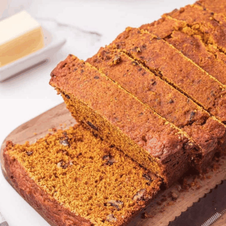 Freshly baked loaf of Easy Cardamom Pumpkin Bread sliced on a wooden board, showing its moist, spiced texture and golden-brown crust.