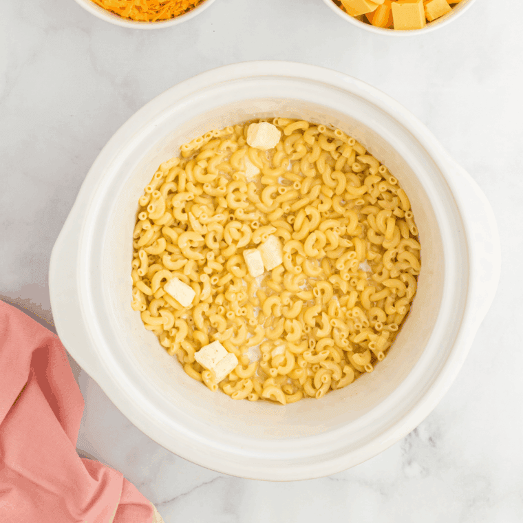 Whisking together milk, butter, flour, and shredded cheddar cheese to make smooth creamy sauce.