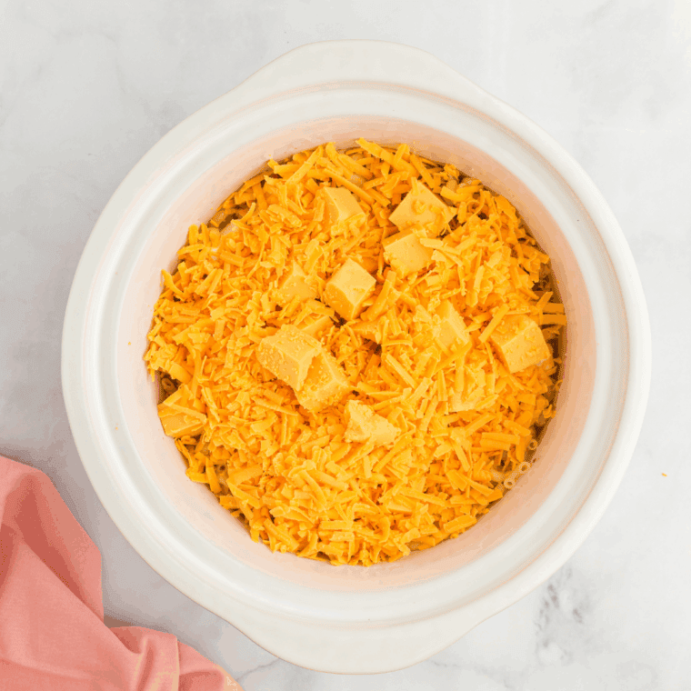 Covering crockpot and cooking mac and cheese on low, stirring occasionally to prevent sticking.