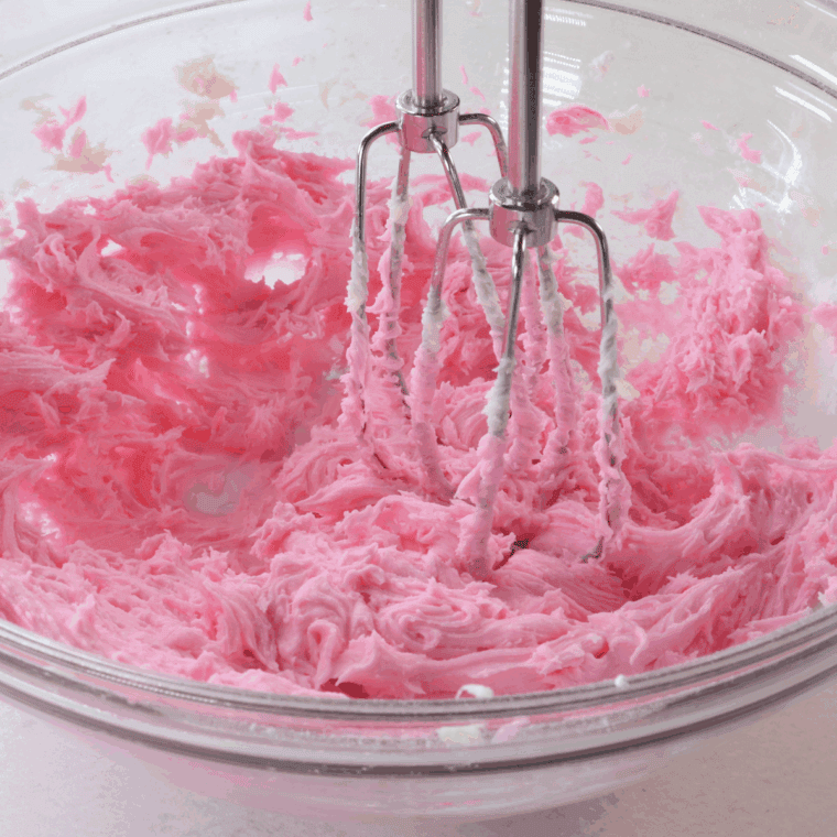 Making pink frosting by mixing butter, powdered sugar, heavy cream, and food coloring"